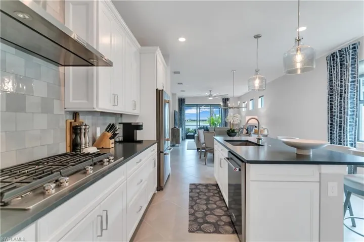 Kitchen featuring white cabinetry, tasteful backsplash, stainless steel appliances, an island with sink, and sink