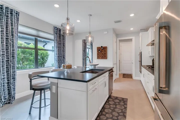 Kitchen with pendant lighting, white cabinetry, stainless steel appliances, sink, and a center island with sink