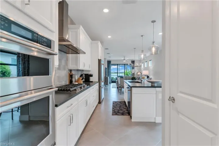 Kitchen featuring stainless steel appliances, ceiling fan, hanging light fixtures, decorative backsplash, and wall chimney range hood