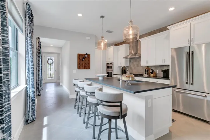 Kitchen featuring stainless steel appliances, white cabinetry, sink, an island with sink, and wall chimney exhaust hood