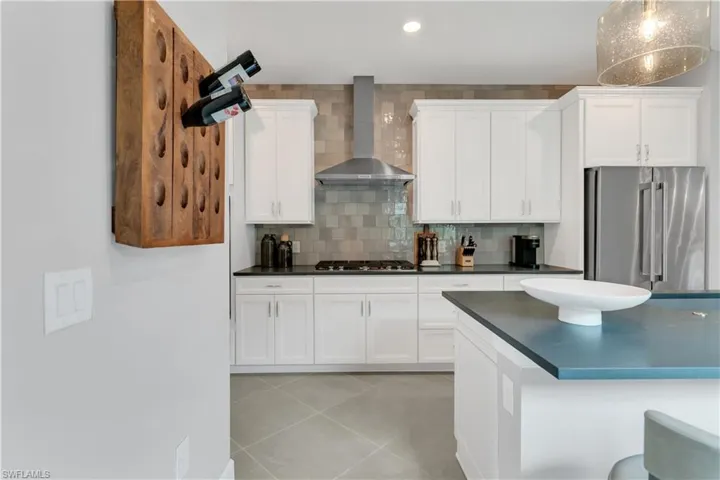 Kitchen with pendant lighting, decorative backsplash, appliances with stainless steel finishes, white cabinets, and wall chimney range hood