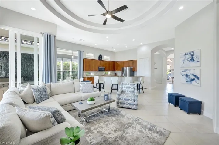 Living area with a raised ceiling, plenty of natural light, recessed lighting, light tile patterned floors, and arched walkways