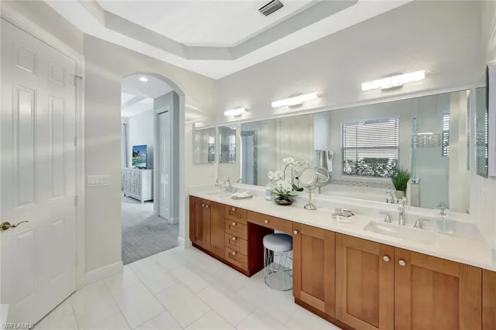Full bathroom featuring a raised ceiling, double vanity, a bath, and light tile patterned flooring