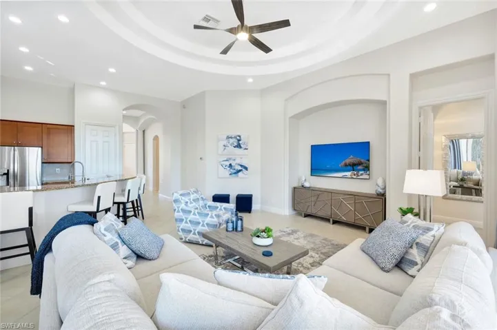 Living area with recessed lighting, light tile patterned floors, arched walkways, ceiling fan, and a tray ceiling