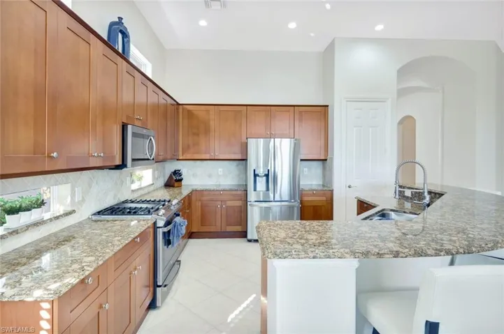 Kitchen featuring stainless steel appliances, brown cabinets, light stone counters, a spacious island, and recessed lighting
