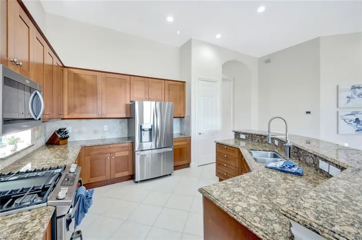 Kitchen with stainless steel appliances, brown cabinets, a center island with sink, tasteful backsplash, and light stone counters