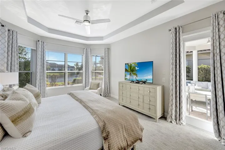 Carpeted bedroom featuring a raised ceiling, multiple windows, a ceiling fan, and access to exterior