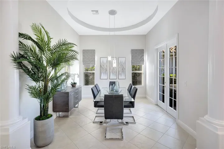 Dining area featuring a raised ceiling, light tile patterned flooring, ornate columns, and french doors