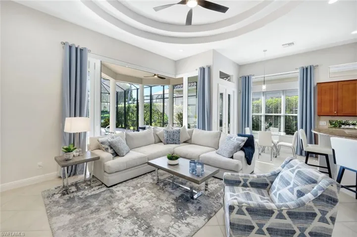 Living area featuring a raised ceiling, light tile patterned floors, and a ceiling fan