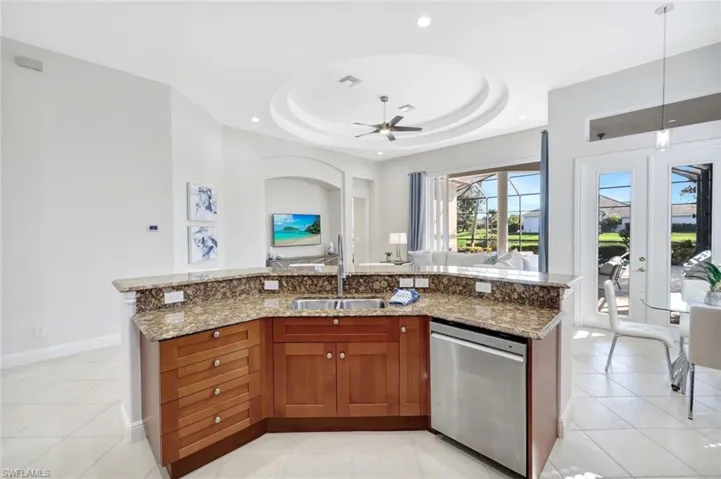 Kitchen with a center island with sink, french doors, light tile patterned floors, dishwasher, and brown cabinetry