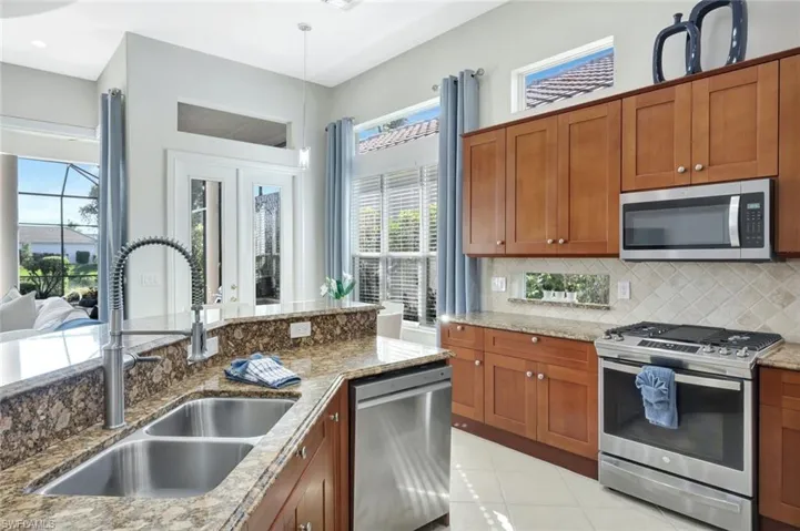 Kitchen featuring stainless steel appliances, brown cabinets, light tile patterned floors, light stone countertops, and pendant lighting