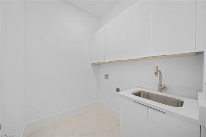 Utility room featuring a stainless steel sink with a brushed nickel faucet, white cabinetry, and light-toned flooring