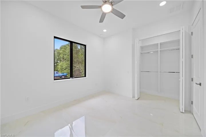 Bright room featuring large format tile flooring, a contemporary ceiling fan, recessed lighting, a spacious built-in closet with shelving and rods, and a black-framed window