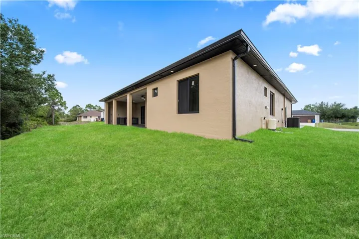 Expansive green lawn bordering a modern stucco exterior with black-framed windows and a covered patio area