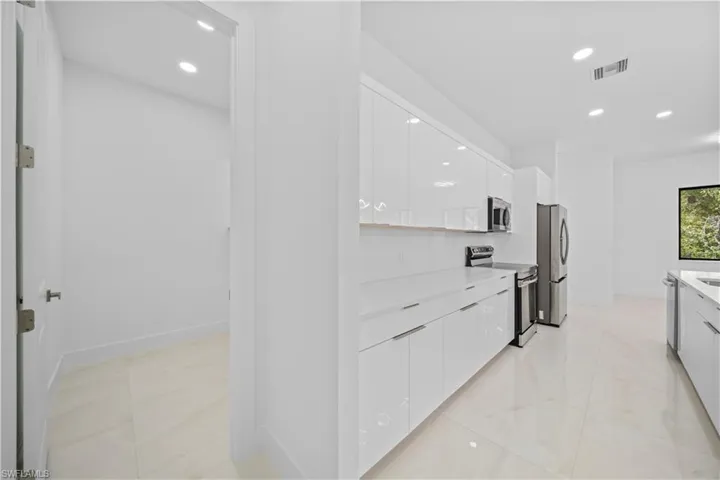 Contemporary kitchen featuring white flat-panel cabinetry, light-toned tile flooring, stainless steel appliances, and recessed lighting