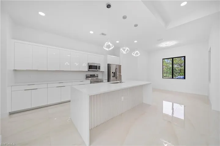 Spacious kitchen featuring an extended island with a waterfall countertop, white flat-panel cabinetry, stainless steel appliances, and large format tile flooring