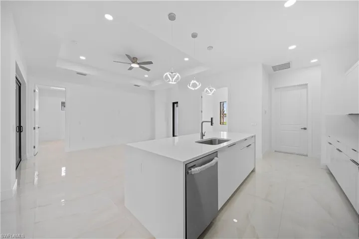 White kitchen island with an integrated stainless steel sink and dishwasher, complemented by recessed lighting and pendant fixtures