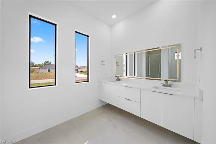 Modern bathroom featuring a double vanity with integrated sinks, white cabinetry, and a large illuminated mirror