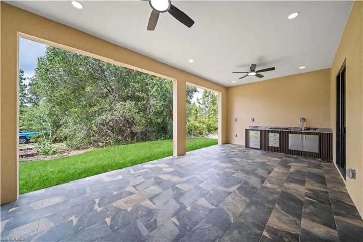 Covered patio featuring slate-style tile flooring, built-in outdoor kitchen with integrated sink and stainless steel appliances, recessed lighting, and dual ceiling fans
