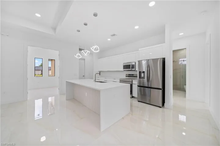Modern kitchen featuring a large island with a quartz countertop, white cabinetry, stainless steel appliances, and polished tile flooring