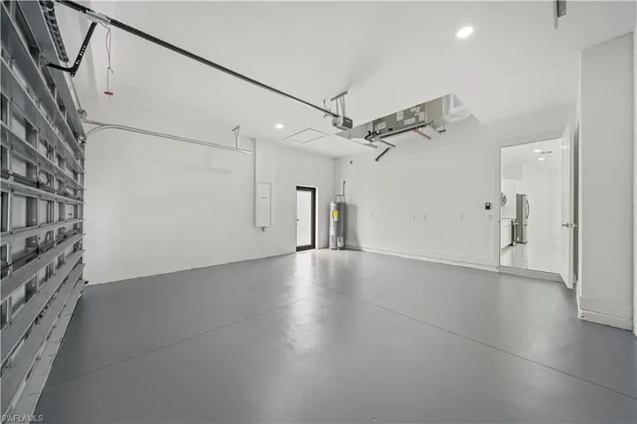 Spacious garage featuring a roll-up door, polished concrete flooring, recessed lighting, a utility door, and a water heater