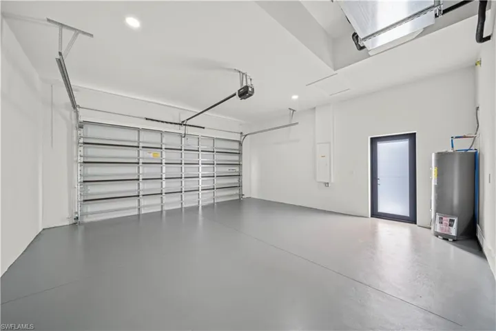 Spacious garage featuring a grey epoxy-coated floor, automatic garage door opener, recessed lighting, and a frosted glass pedestrian door