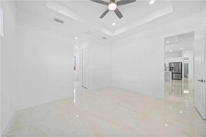 Spacious room featuring large format polished tile flooring, a tray ceiling with recessed lighting, and a ceiling fan