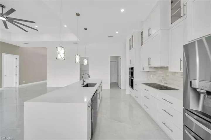Kitchen featuring a kitchen island with sink, a sink, a ceiling fan, appliances with stainless steel finishes, and decorative backsplash