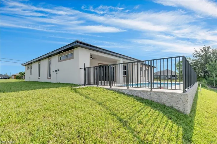 Rear view of property with ceiling fan, a yard, a fenced in pool, and stucco siding