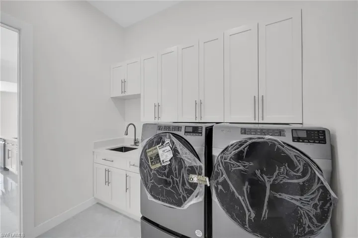 Laundry room with washing machine and dryer, cabinet space, a sink, and baseboards