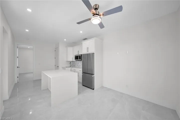 Kitchen featuring white cabinets, a center island, light countertops, stainless steel appliances, and a sink