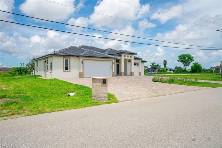 Prairie-style home with a tile roof, an attached garage, decorative driveway, a front yard, and stucco siding