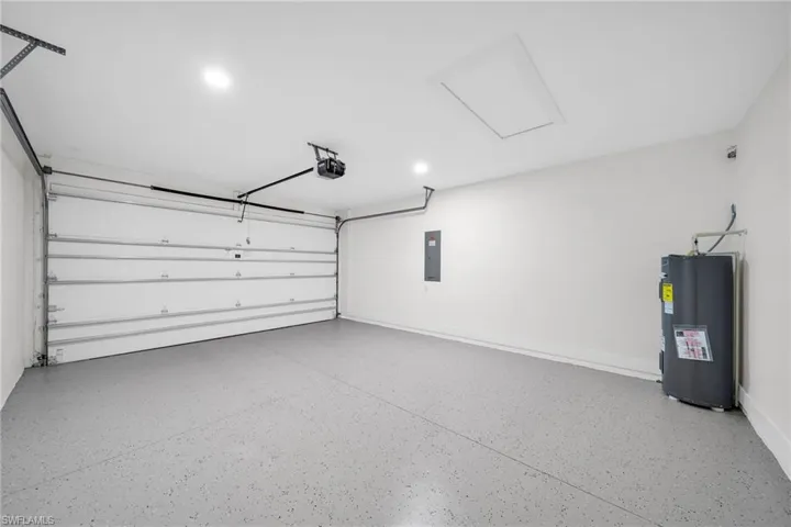 Garage featuring electric panel, baseboards, a garage door opener, and electric water heater