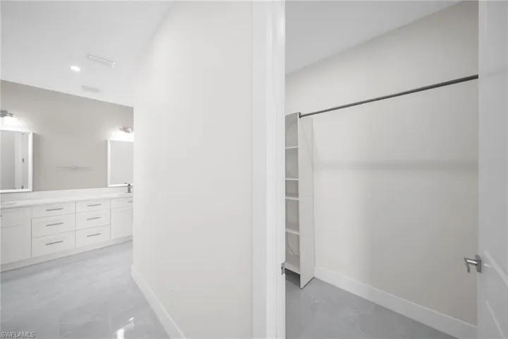 Full bathroom with double vanity, marble finish floor, a spacious closet, and baseboards
