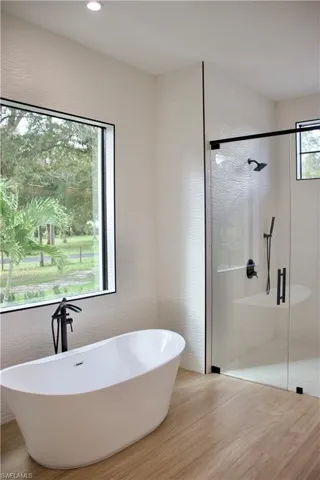 Full bath featuring a shower stall, a soaking tub, tile walls, wood finished floors, and recessed lighting