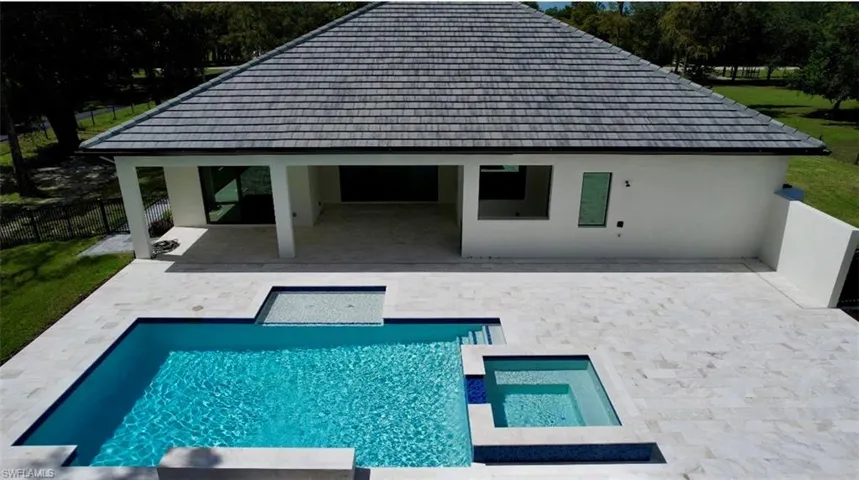 Rear view of house with stucco siding, a patio, a pool with connected hot tub, and a fenced backyard