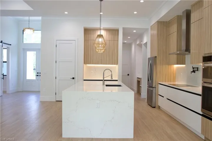 Kitchen featuring a barn door, wall chimney range hood, light stone counters, modern cabinets, and crown molding
