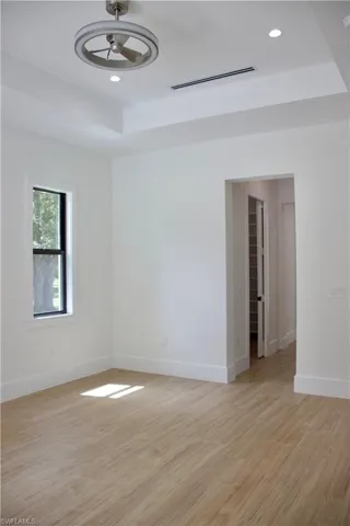 Spare room with light wood-style floors, a tray ceiling, recessed lighting, and a ceiling fan