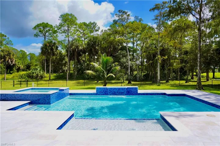 View of swimming pool with a lawn, a patio, a pool with connected hot tub, and view of wooded area