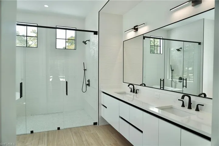 Full bathroom featuring a shower stall, double vanity, and light wood-style flooring