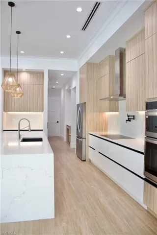 Kitchen with modern cabinets, light brown cabinetry, decorative light fixtures, light stone countertops, and recessed lighting