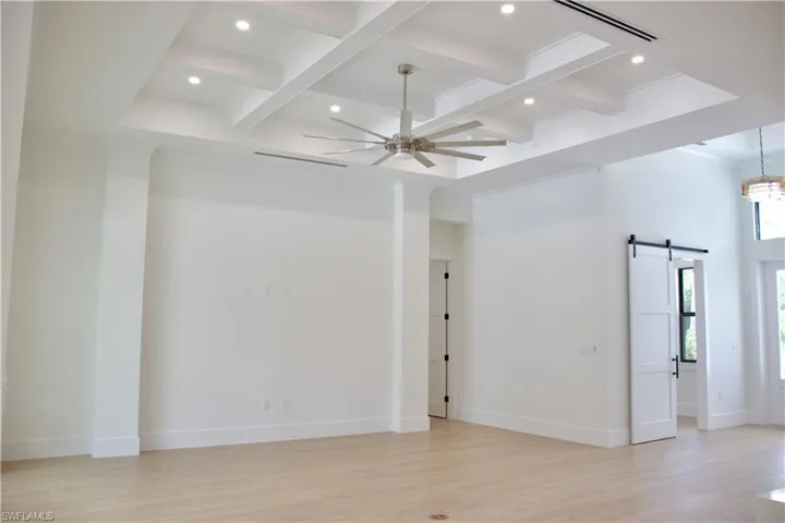 Empty room with a barn door, beamed ceiling, coffered ceiling, light wood-style floors, and recessed lighting