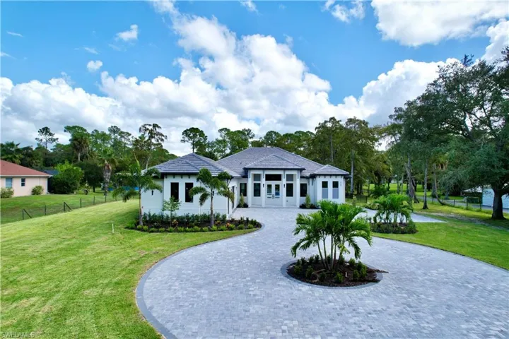 View of front of property featuring curved driveway, stucco siding, and view of scattered trees