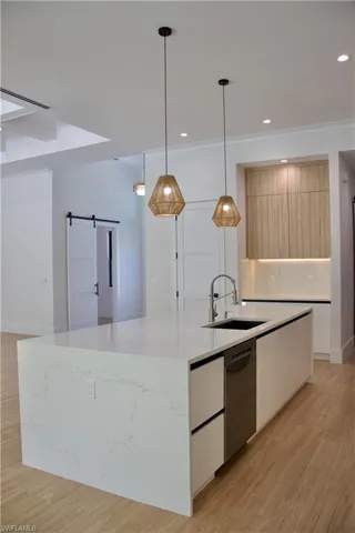 Kitchen featuring a barn door, modern cabinets, white cabinetry, a spacious island, and hanging light fixtures