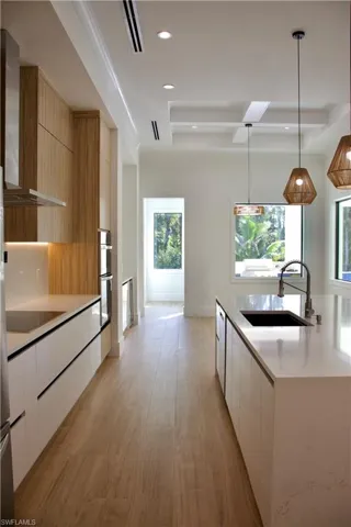 Kitchen with modern cabinets, pendant lighting, light wood-style floors, wall chimney range hood, and recessed lighting
