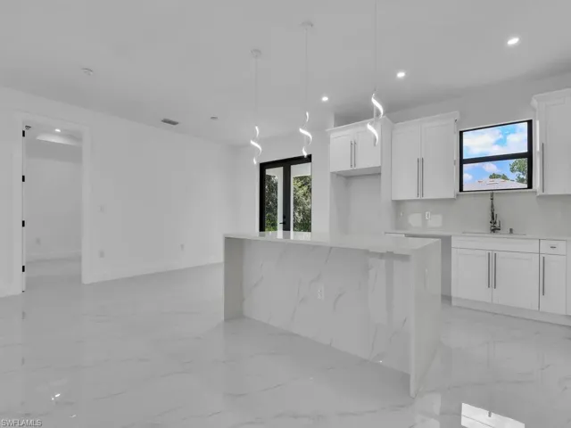 Kitchen featuring light tile patterned floors, white cabinets, a kitchen island, decorative light fixtures, and sink