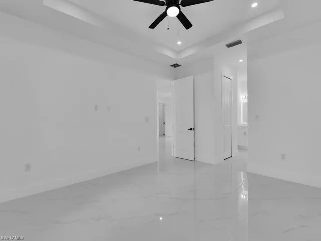 Tiled empty room with ceiling fan and a tray ceiling