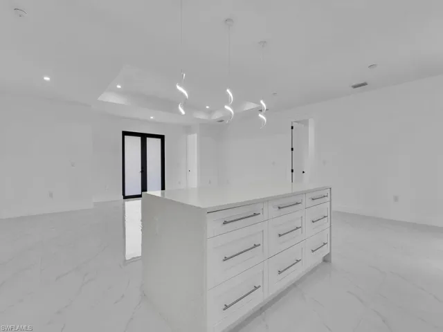 Kitchen featuring decorative light fixtures, white cabinetry, a tray ceiling, a kitchen island, and light tile patterned floors
