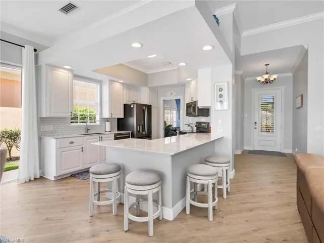 Kitchen with a kitchen bar, backsplash, ornamental molding, white cabinets, and a peninsula