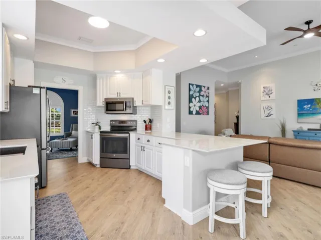 Kitchen featuring ornamental molding, open floor plan, a peninsula, stainless steel appliances, and a kitchen breakfast bar